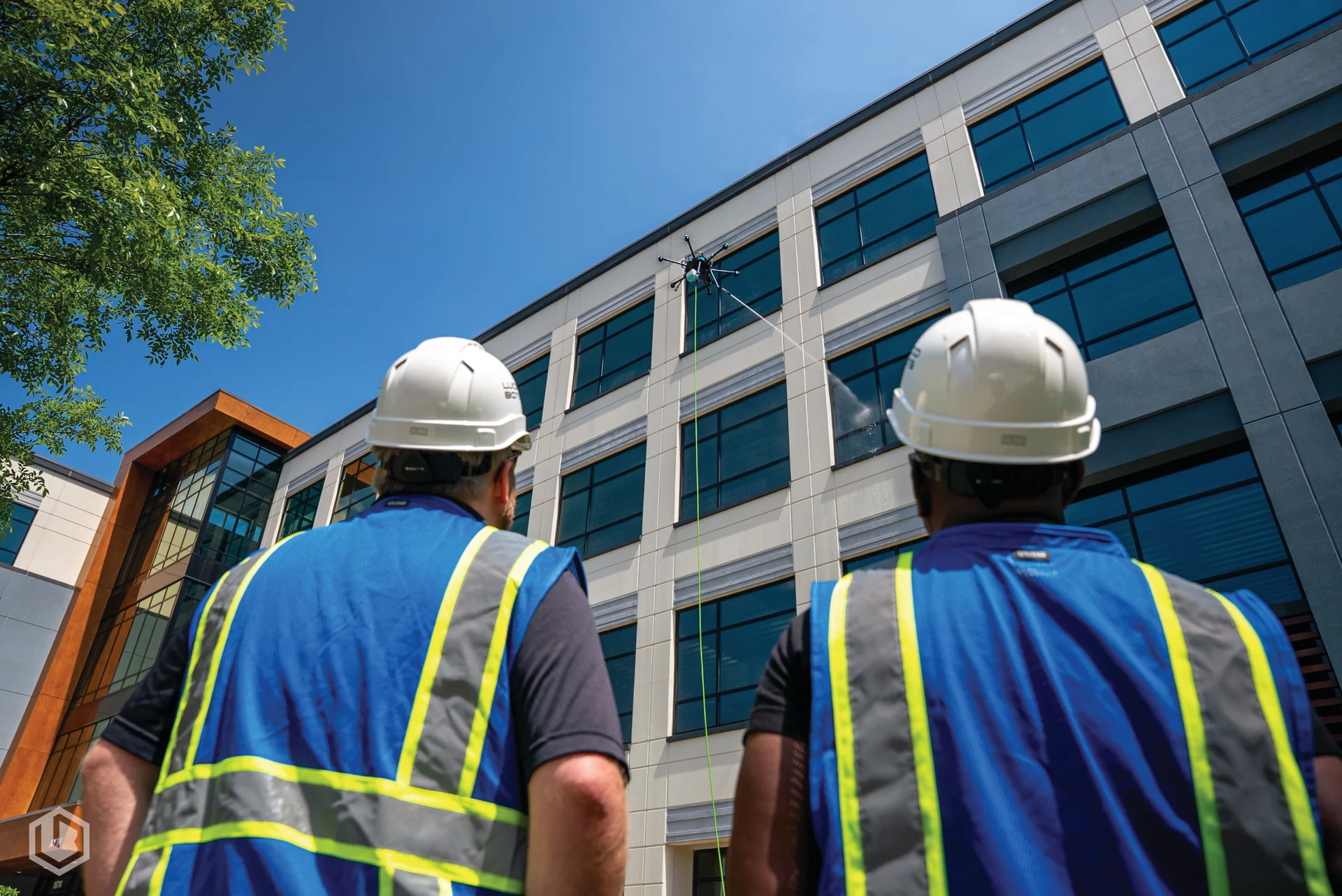 Two hardhat-wearing technicians watching a drone clean a commercial building